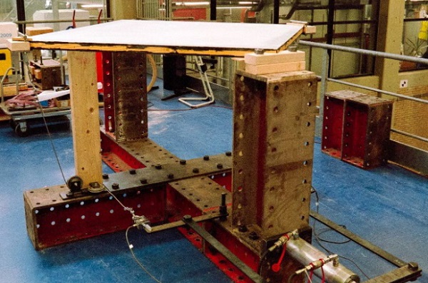 Fig. 7: The set-up of the experiments.The manually actuated hydraulic cylinder is visible on the bottom right. Note the mechanism of bars, cables and pulleys that is used to get the load to the corner of the panel.